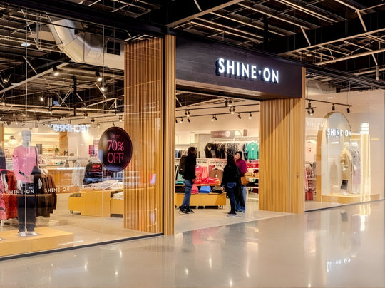 Storefront of 'SHINE ON' with people inside, displaying products and promotional signs.